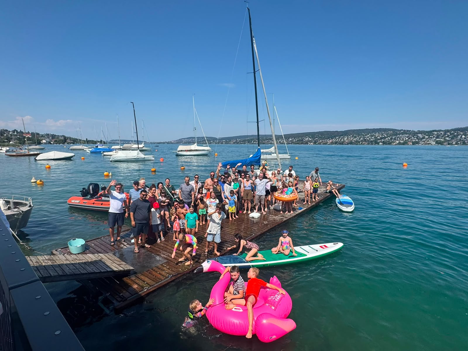Grosse Gruppe von Familien auf dem Steg der Seglervereinigung Thalwil am Zürichsee, Kinder auf SUP-Boards und einem pinken Flamingo im Wasser